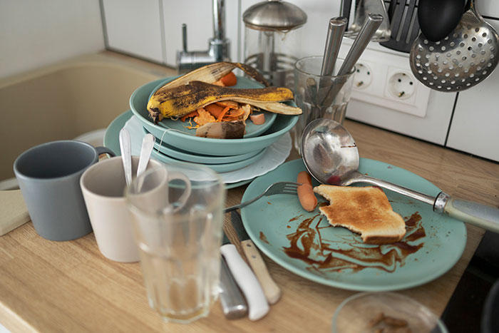 Dirty dishes and leftover food clutter a kitchen sink area, depicting signs of possible laziness or neglect. Dirty dishes and leftover food clutter a kitchen sink area, depicting signs of possible laziness or neglect.