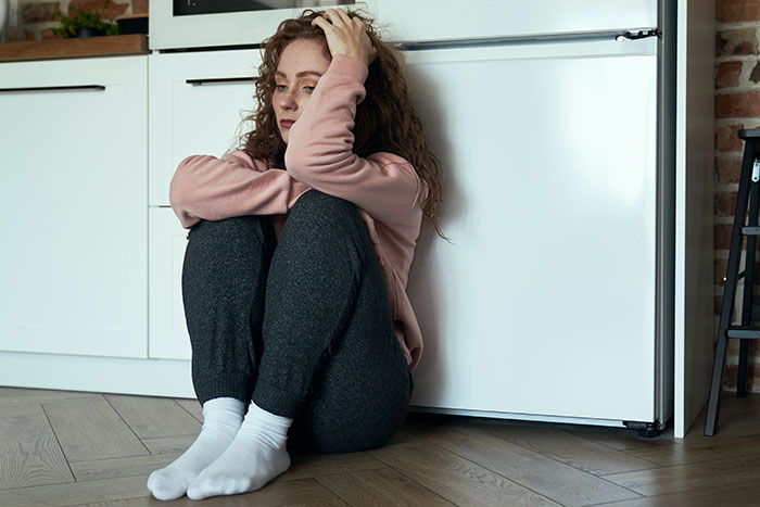 Young woman sitting on the floor, hugging knees and looking upset, illustrating depressed is not an excuse for being lazy. Young woman sitting on the floor, hugging knees and looking upset, illustrating depressed is not an excuse for being lazy.