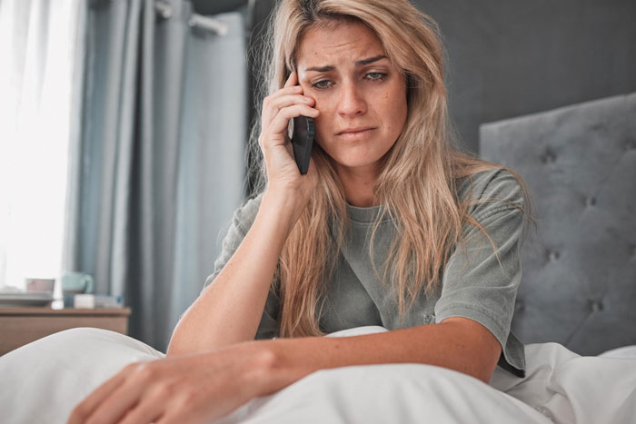 Worried woman on phone sitting in bed, reflecting on issues involving criminal ex and troubled relationship. Worried woman on phone sitting in bed, reflecting on issues involving criminal ex and troubled relationship.
