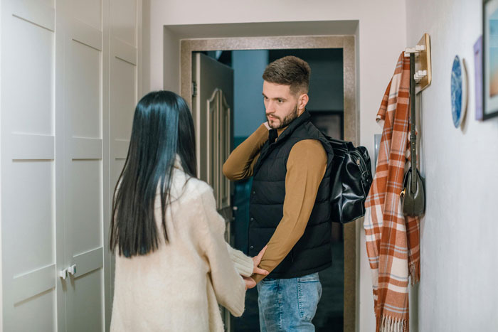 Couple in a tense conversation at home, boyfriend hesitating with travel bag, girlfriend holding his hands, relationship doubts. Couple in a tense conversation at home, boyfriend hesitating with travel bag, girlfriend holding his hands, relationship doubts.