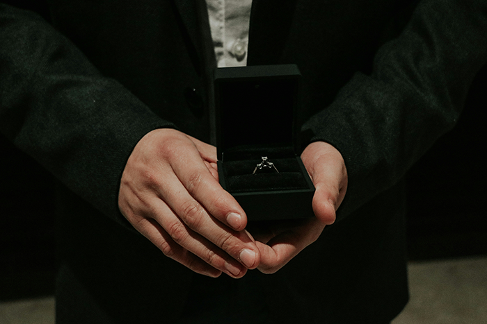 Man in dark suit holding an engagement ring box, symbolizing a proposal with an open marriage twist. Man in dark suit holding an engagement ring box, symbolizing a proposal with an open marriage twist.