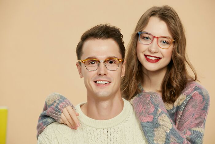 Young couple wearing glasses and cozy sweaters, smiling in a warm setting illustrating shocking dark secrets concept.