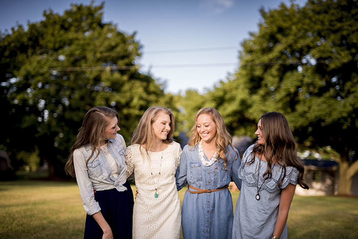Four women standing outdoors smiling and talking, capturing a sister revealed dead brother lie moment in a sunny park.