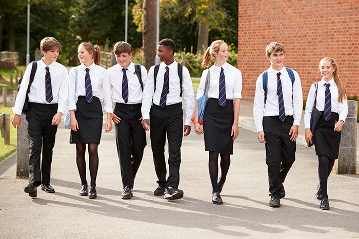 Group of teenage students in boarding school uniforms walking outside on campus on a sunny day