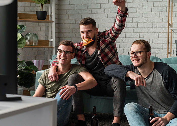 Three men watching TV and enjoying pizza and drinks, highlighting masculinity so fragile in social settings. Three men watching TV and enjoying pizza and drinks, highlighting masculinity so fragile in social settings.
