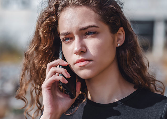 Young woman with curly hair looking uncomfortable while talking on phone outdoors, reflecting fragile masculinity issues. Young woman with curly hair looking uncomfortable while talking on phone outdoors, reflecting fragile masculinity issues.