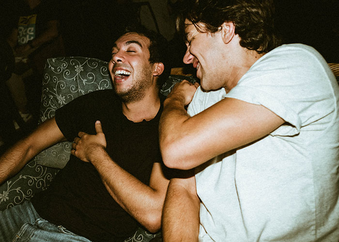Two young men laughing together at a casual gathering, highlighting themes of masculinity and social discomfort. Two young men laughing together at a casual gathering, highlighting themes of masculinity and social discomfort.