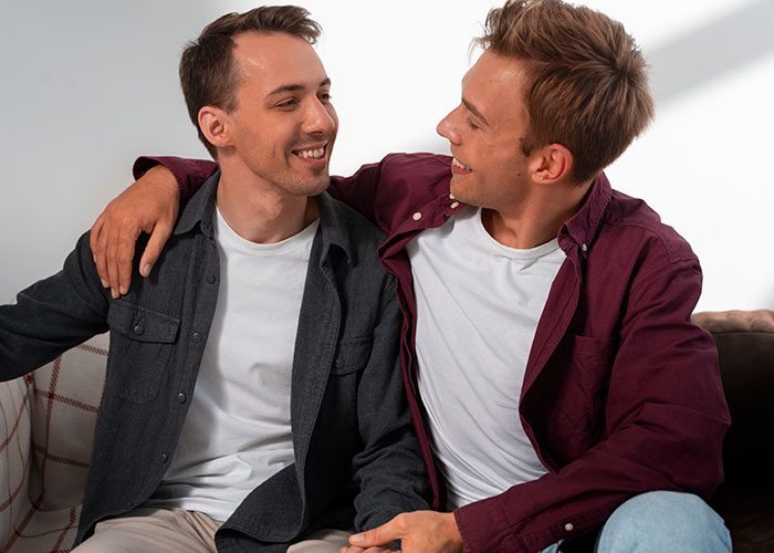 Two men sitting closely on a couch, smiling and showing a moment of connection related to masculinity so fragile concept. Two men sitting closely on a couch, smiling and showing a moment of connection related to masculinity so fragile concept.