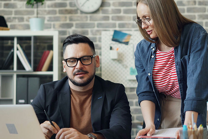 Man and woman with glasses discussing hard truths women realize while working together in a modern office setting