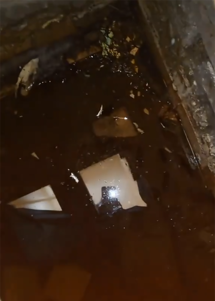 Dark hidden space under floor with water and debris, revealing secret feature discovered by woman in new home.