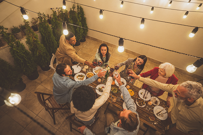Group of friends enjoying dinner party outdoors with string lights, raising glasses in a toast, capturing obnoxious dinner guest husband dread. Group of friends enjoying dinner party outdoors with string lights, raising glasses in a toast, capturing obnoxious dinner guest husband dread.