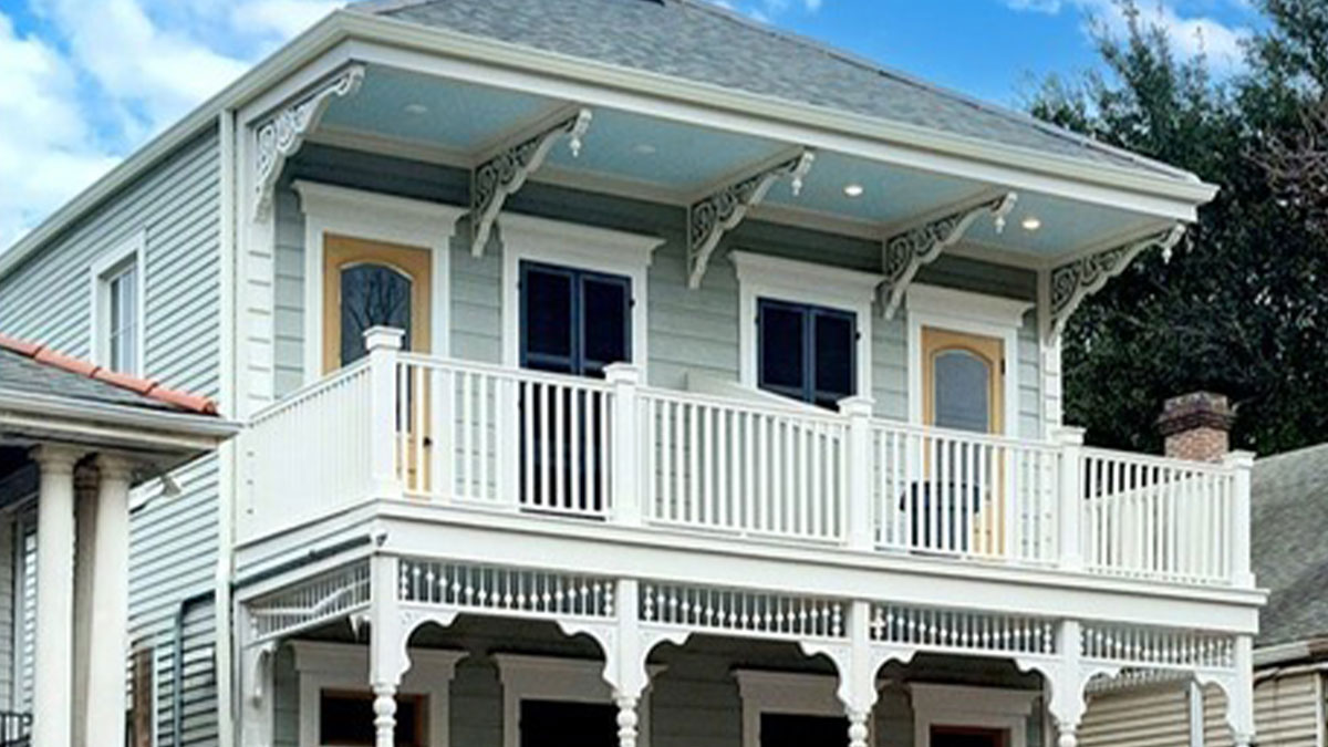 Two-story house restored to historical glory with detailed trim, upper balcony, and classic wooden exterior in soft colors.
