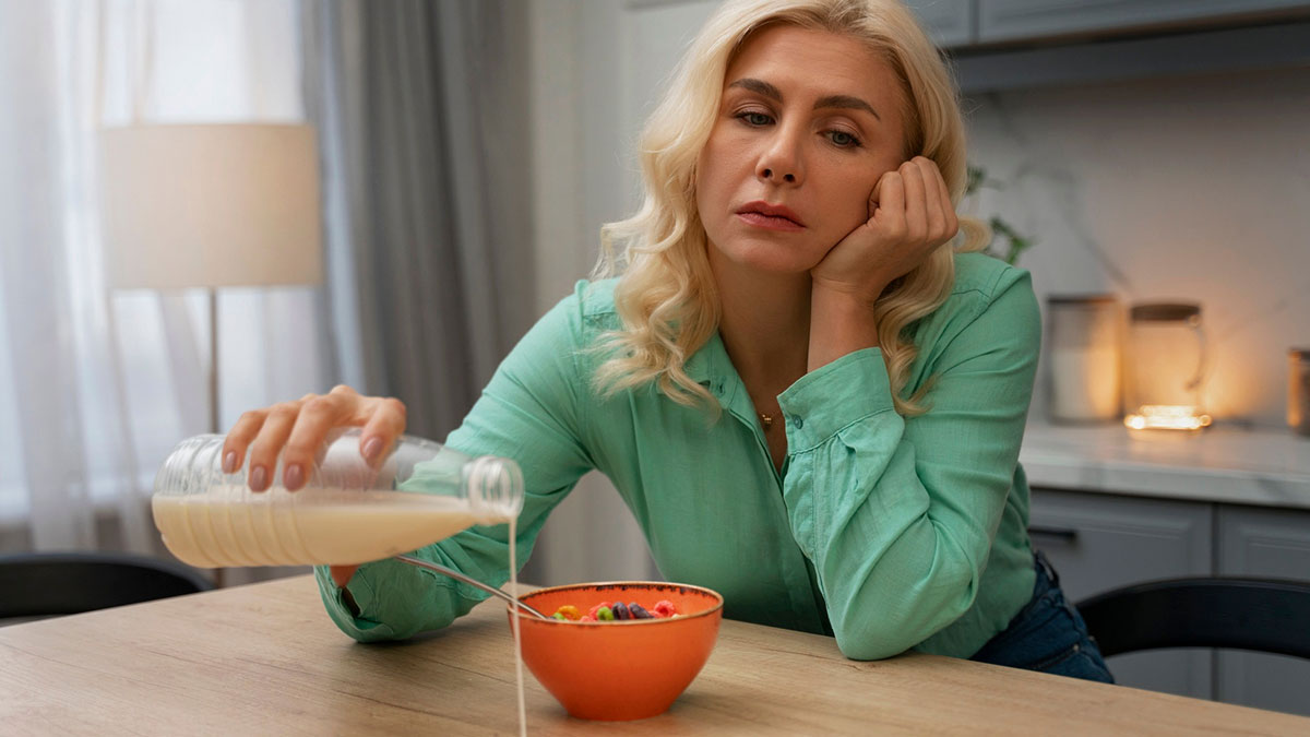 Mom feeling frustrated pouring milk into cereal alone at the kitchen table, reflecting struggle to eat together with family