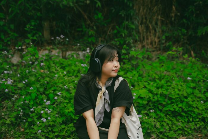 Teen girl wearing headphones sitting outdoors surrounded by greenery, reflecting on popular kids who became outcasts in school.