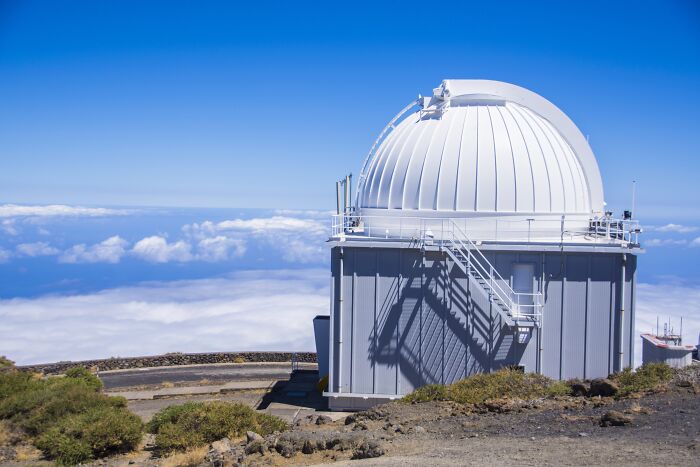Observatory dome on mountain top under clear blue sky with people sharing potentially dangerous situations nearby.