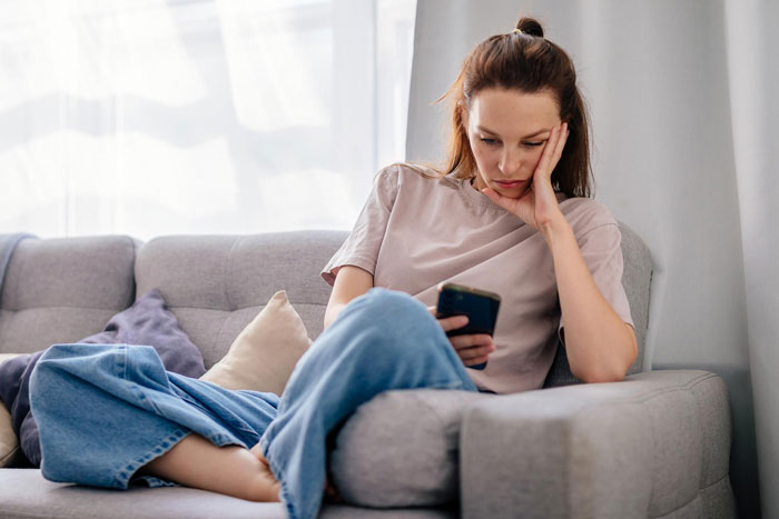 Young woman looking worried on couch, holding phone, reflecting concern about slacker hubby plans after wife's surgery. Young woman looking worried on couch, holding phone, reflecting concern about slacker hubby plans after wife's surgery.