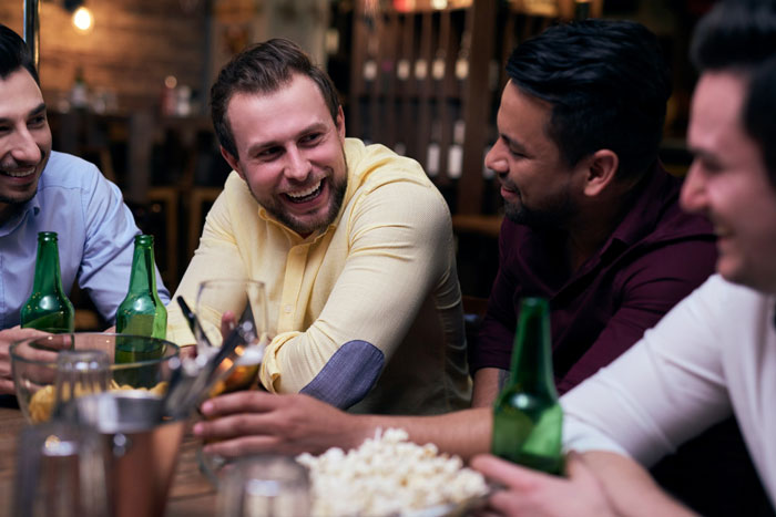 Group of men casually chatting and drinking at a bar, reflecting slacker hubby planning to skip caring for wife after surgery. Group of men casually chatting and drinking at a bar, reflecting slacker hubby planning to skip caring for wife after surgery.