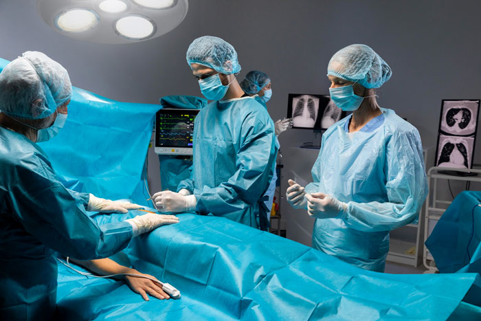 Surgical team performing operation in a sterile operating room with medical equipment and lung X-rays visible. Surgical team performing operation in a sterile operating room with medical equipment and lung X-rays visible.