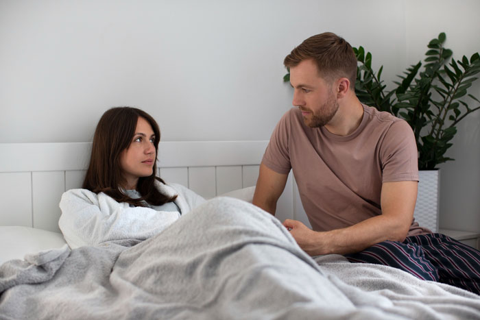 Man sitting beside wife in bed looking concerned, illustrating slacker hubby plans to skip care after surgery. Man sitting beside wife in bed looking concerned, illustrating slacker hubby plans to skip care after surgery.