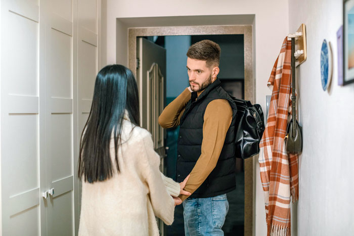 Man with backpack looking reluctant while woman in white sweater holds his hand indoors, reflecting a slacker hubby scenario. Man with backpack looking reluctant while woman in white sweater holds his hand indoors, reflecting a slacker hubby scenario.