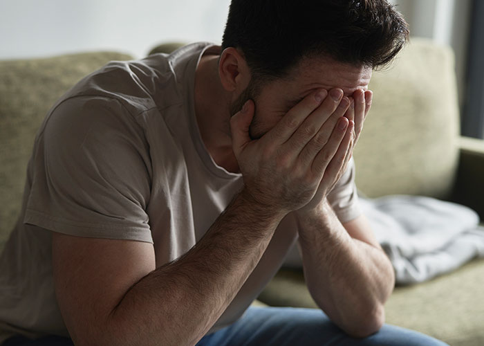 Man sitting on a couch covering his face in distress after womanâs dream of tummy tuck is shattered by lost savings. Man sitting on a couch covering his face in distress after womanâs dream of tummy tuck is shattered by lost savings.