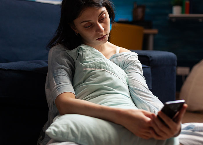 Woman upset sitting on floor hugging pillow, looking at phone, reflecting on lost tummy tuck savings after husband's betrayal. Woman upset sitting on floor hugging pillow, looking at phone, reflecting on lost tummy tuck savings after husband's betrayal.