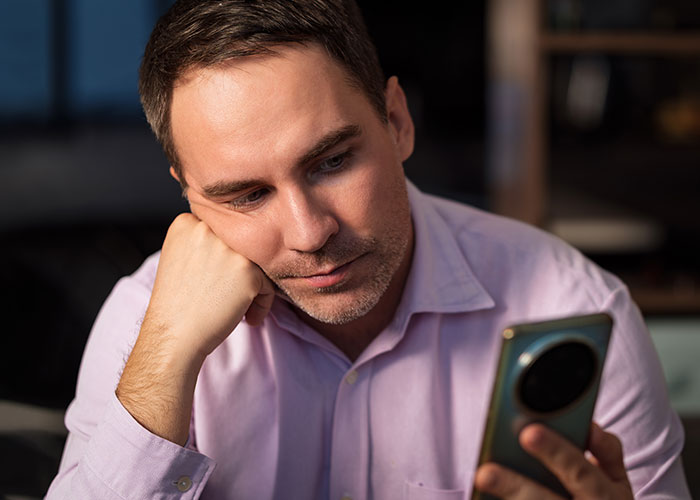 Man in a pink shirt looking thoughtfully at his smartphone, reflecting on a womanâs dream of having a tummy tuck. Man in a pink shirt looking thoughtfully at his smartphone, reflecting on a womanâs dream of having a tummy tuck.