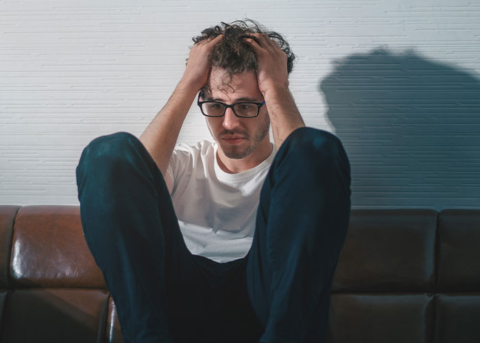 Man sitting on a couch with hands in hair, looking stressed and upset about lost savings for tummy tuck dreams. Man sitting on a couch with hands in hair, looking stressed and upset about lost savings for tummy tuck dreams.