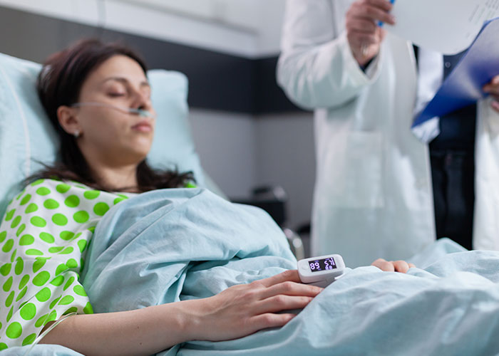 Woman lying in hospital bed with oxygen tube and fingertip pulse oximeter, relating to tummy tuck savings loss story Woman lying in hospital bed with oxygen tube and fingertip pulse oximeter, relating to tummy tuck savings loss story