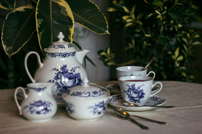 Porcelain tea set with blue floral patterns displayed on a table amid green plants in a cozy setting. Porcelain tea set with blue floral patterns displayed on a table amid green plants in a cozy setting.