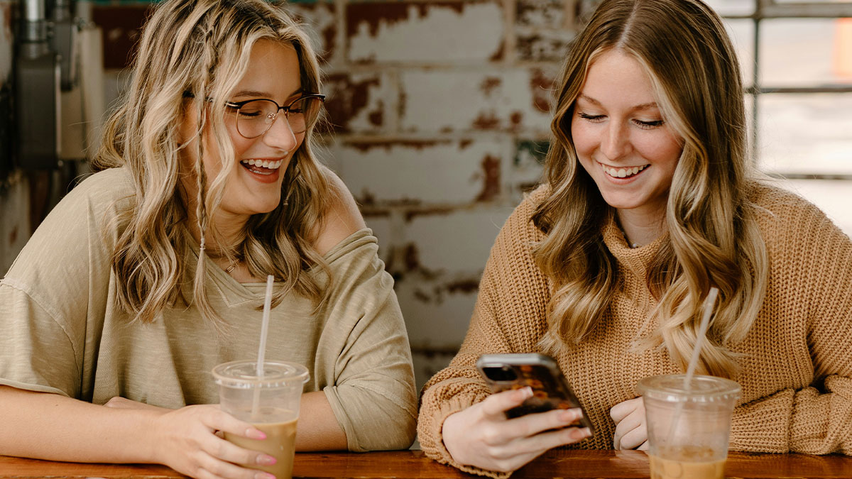 Two women smiling and looking at a phone, sharing a moment of pro revenge on cheating boyfriend stories.