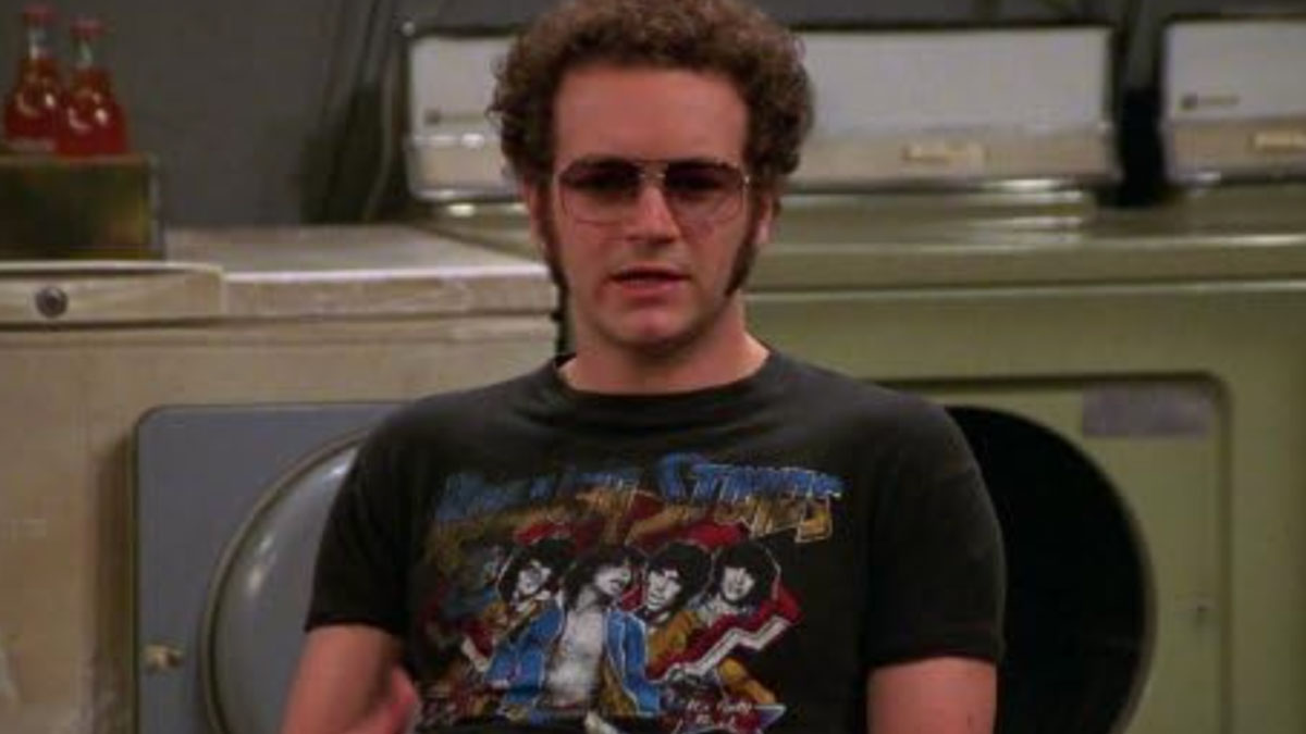 Young man wearing sunglasses and a Rolling Stones shirt in a laundromat, illustrating disappointment in someone idolized.