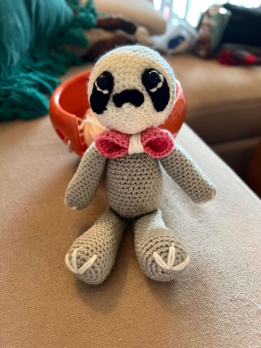 Crochet animal sloth with black eyes and pink bow sitting on a table showcasing personality in handmade toy collection.