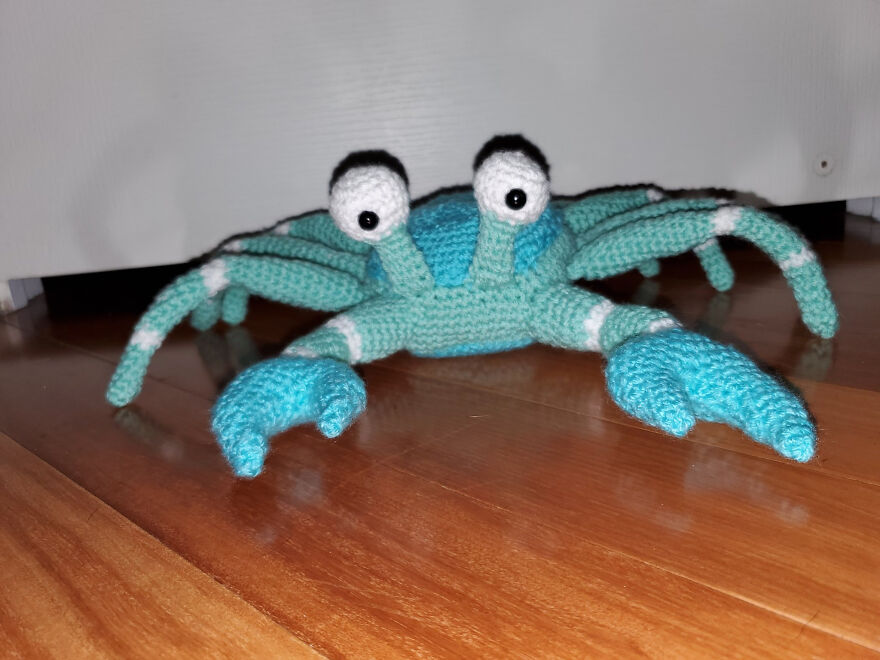 Crochet crab with large eyes and detailed claws sitting on a wooden floor showcasing crochet animals with personality.