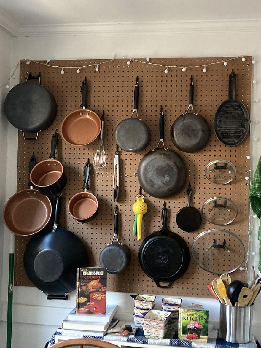 Kitchen pans and utensils organized neatly on a pegboard wall showcasing organization hacks for home spaces.