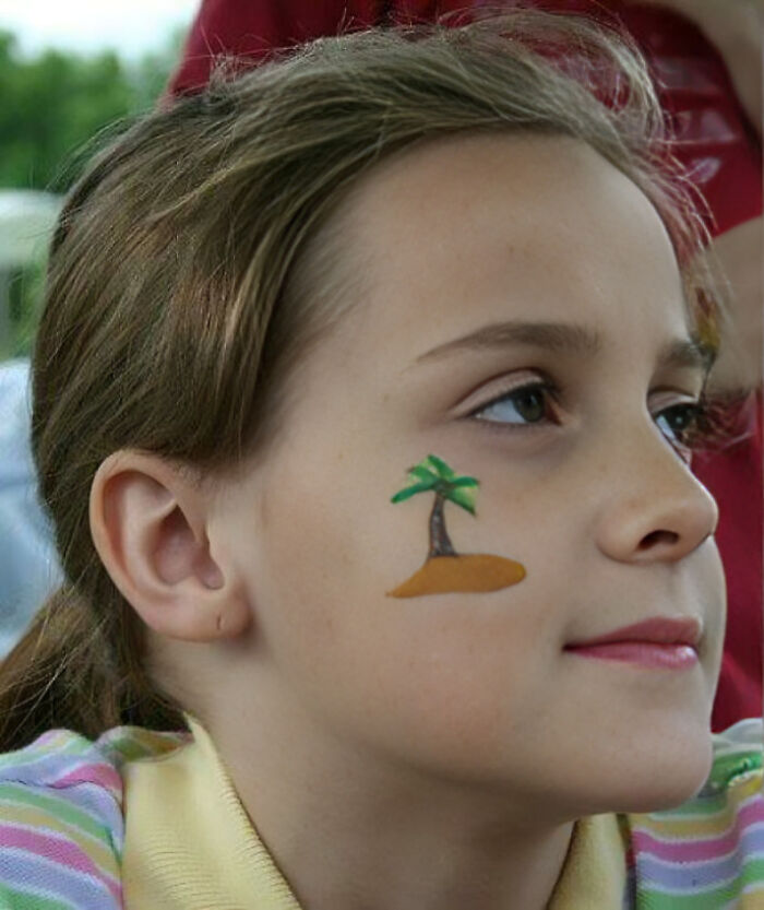 Close-up of a girl with a painted palm tree on her cheek, illustrating unhinged pics of people doing exactly what they were asked to do.