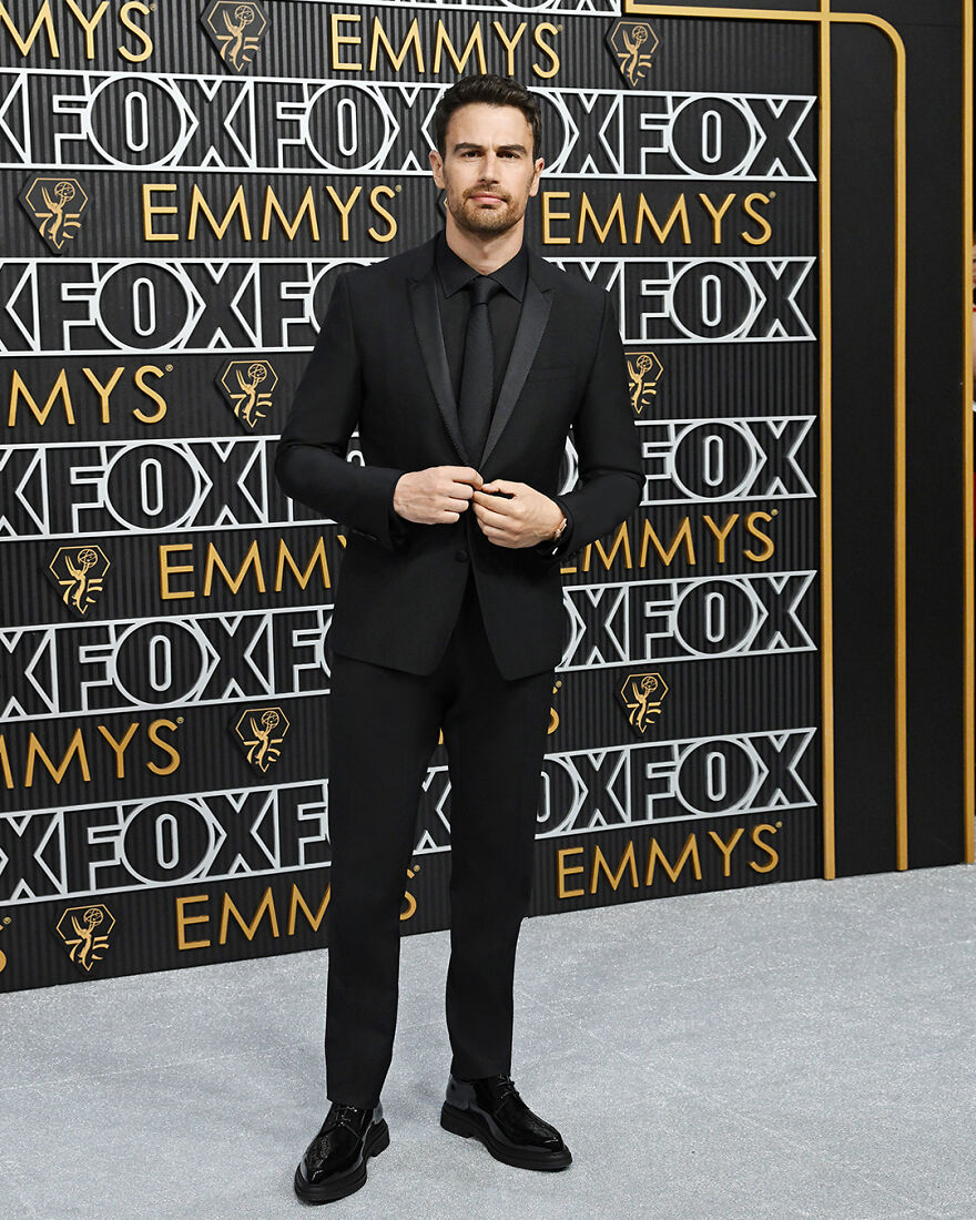 Theo James in a black suit posing on red carpet at awards event, representing most handsome man in the world 2025.