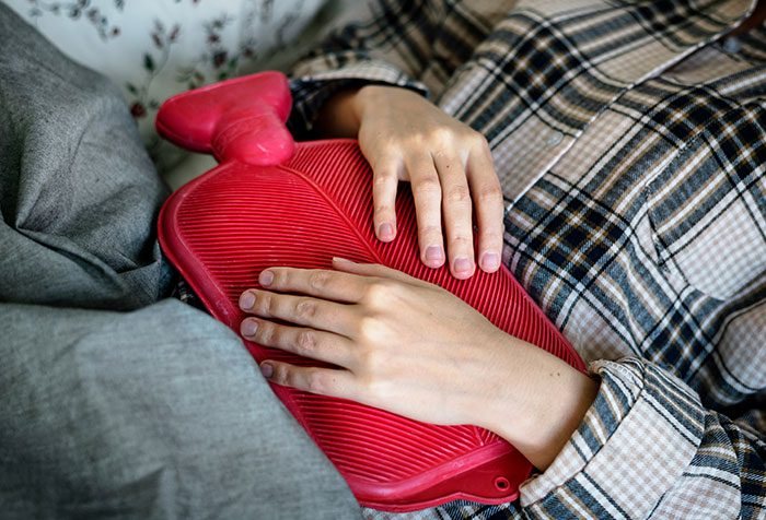 Person holding a red hot water bottle on their stomach, illustrating cases of people self-diagnosing correctly.