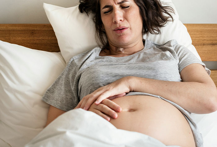 Woman lying in bed holding her abdomen in pain, illustrating cases of people self-diagnosing correctly despite doctors' doubts.