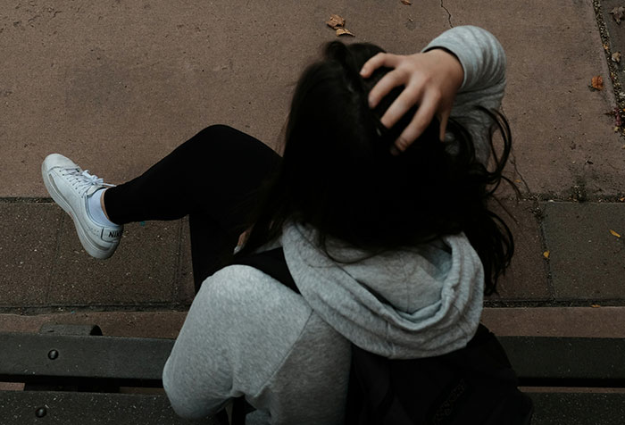 Person in gray hoodie sitting on bench, holding head, illustrating self-diagnosed health cases with initial medical disbelief.
