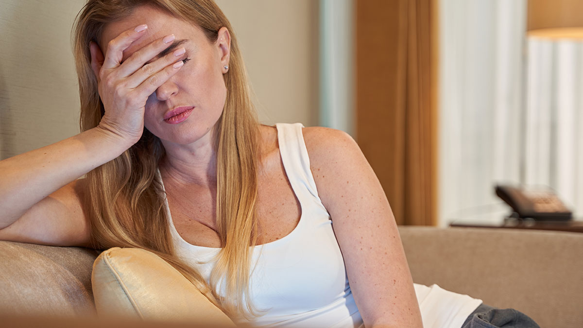 Woman stressed and upset on couch, holding face, symbolizing relationship tension after family sides with creepy brother-in-law.