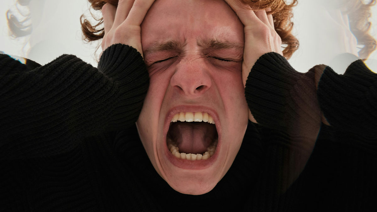 Person wearing black sweater holding their head and screaming in frustration, showing mild infuriating things testing patience.