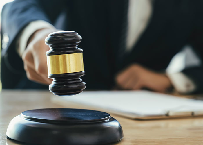 Judge's wooden gavel with gold band striking sound block during legal proceedings in a courtroom setting.