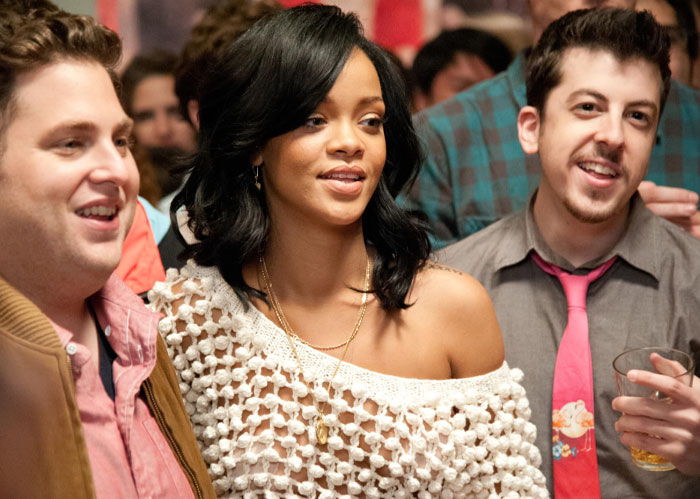 Rihanna socializing with friends at a lively party, wearing a white crocheted top and gold necklace.
