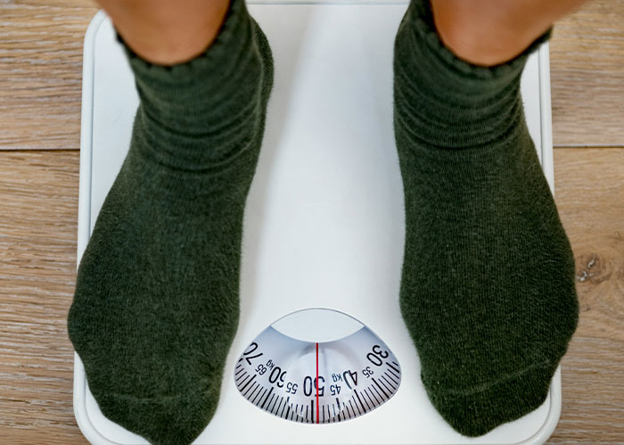 Person wearing dark socks standing on a white scale showing weight, related to Rihanna Slapped Him facts.