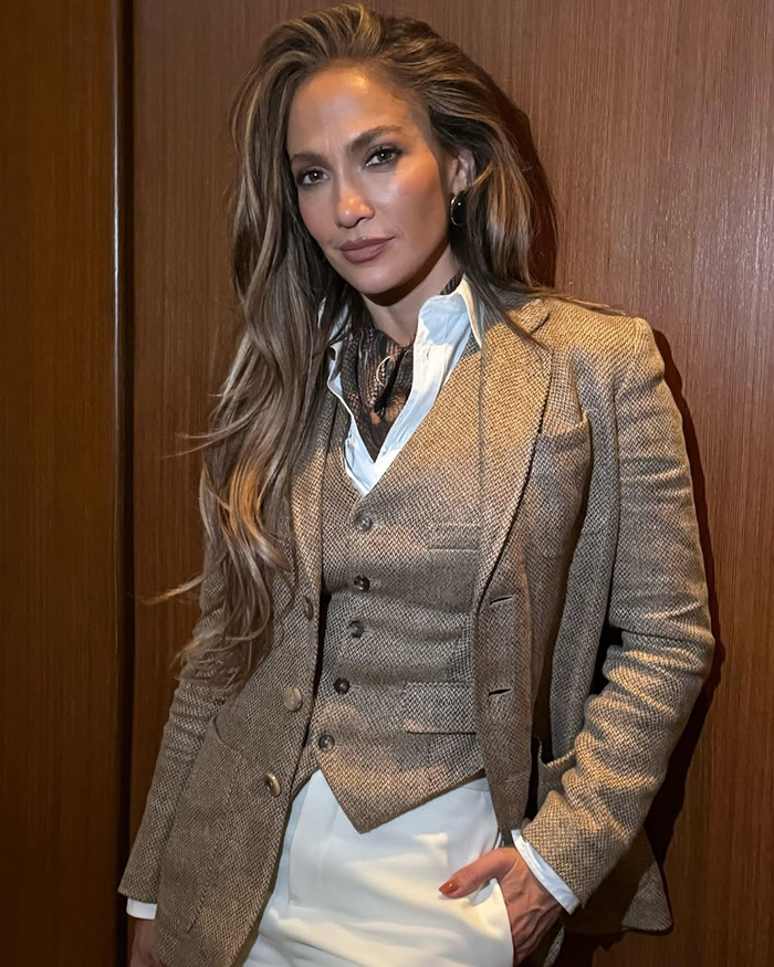Jennifer Lopez wearing a beige suit jacket and vest, posing confidently against a wooden backdrop. Jennifer Lopez wearing a beige suit jacket and vest, posing confidently against a wooden backdrop.
