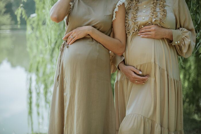 Two pregnant women standing outdoors, gently holding their baby bumps in a serene, natural setting. Two pregnant women standing outdoors, gently holding their baby bumps in a serene, natural setting.