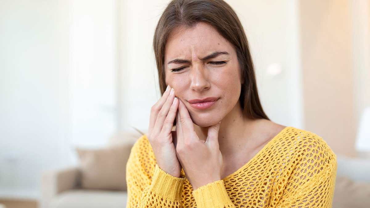 Young woman in yellow sweater holding her jaw in pain, illustrating anxiety symptoms that can be signs of something serious.