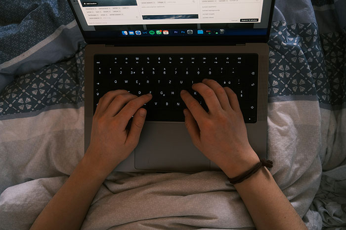 Person typing on a laptop keyboard in bed, highlighting creepy discovery of secret photos after weeks of dating. Person typing on a laptop keyboard in bed, highlighting creepy discovery of secret photos after weeks of dating.