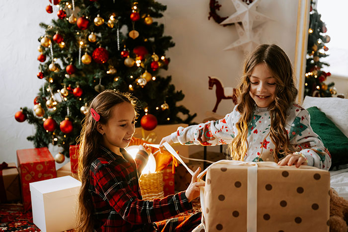 Two girls happily opening presents by a decorated Christmas tree, capturing a family moment with kid’s photos and gifts. Two girls happily opening presents by a decorated Christmas tree, capturing a family moment with kid’s photos and gifts.